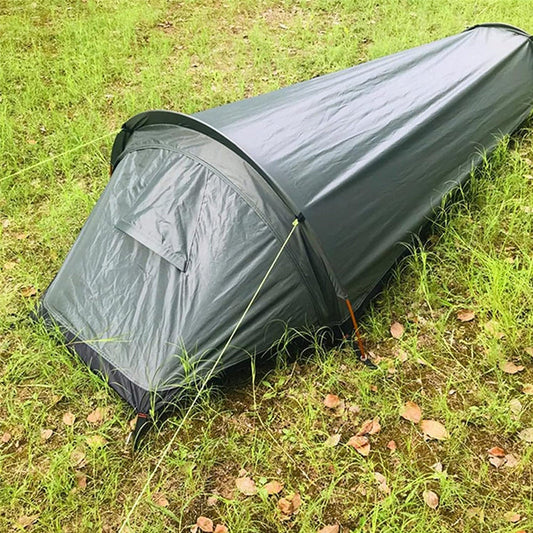 A compact, solo lightweight camping tent set up on a grassy field, displaying its low-profile, weather-resistant design for backpacking and backcountry survival.