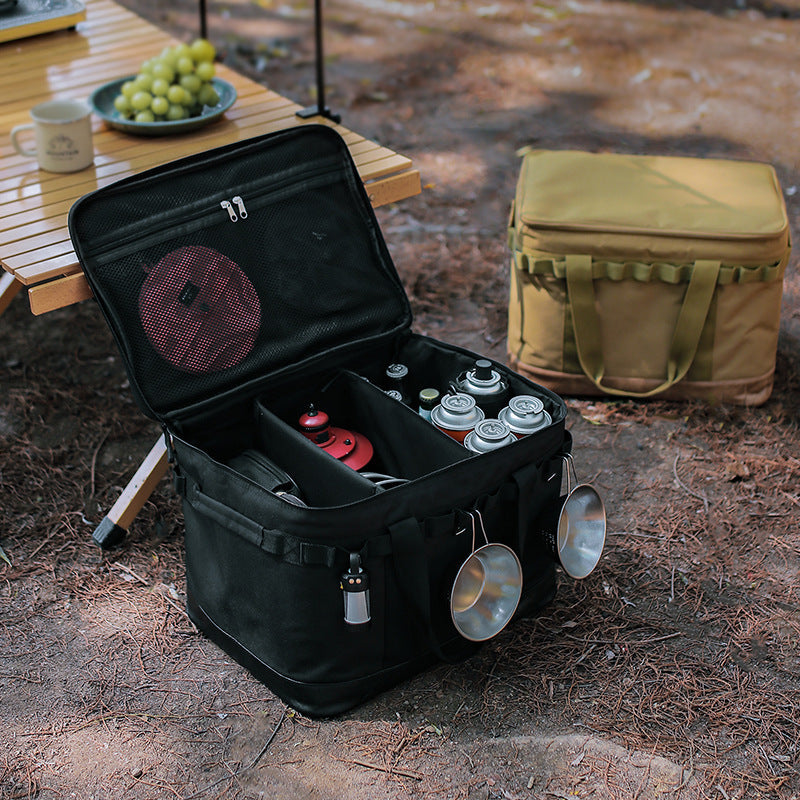 An AlphaLife247 multifunctional black storage box, shown in an outdoor setting, loaded with camping tableware and gear, highlighting its boxy, organized design for expedition logistics.