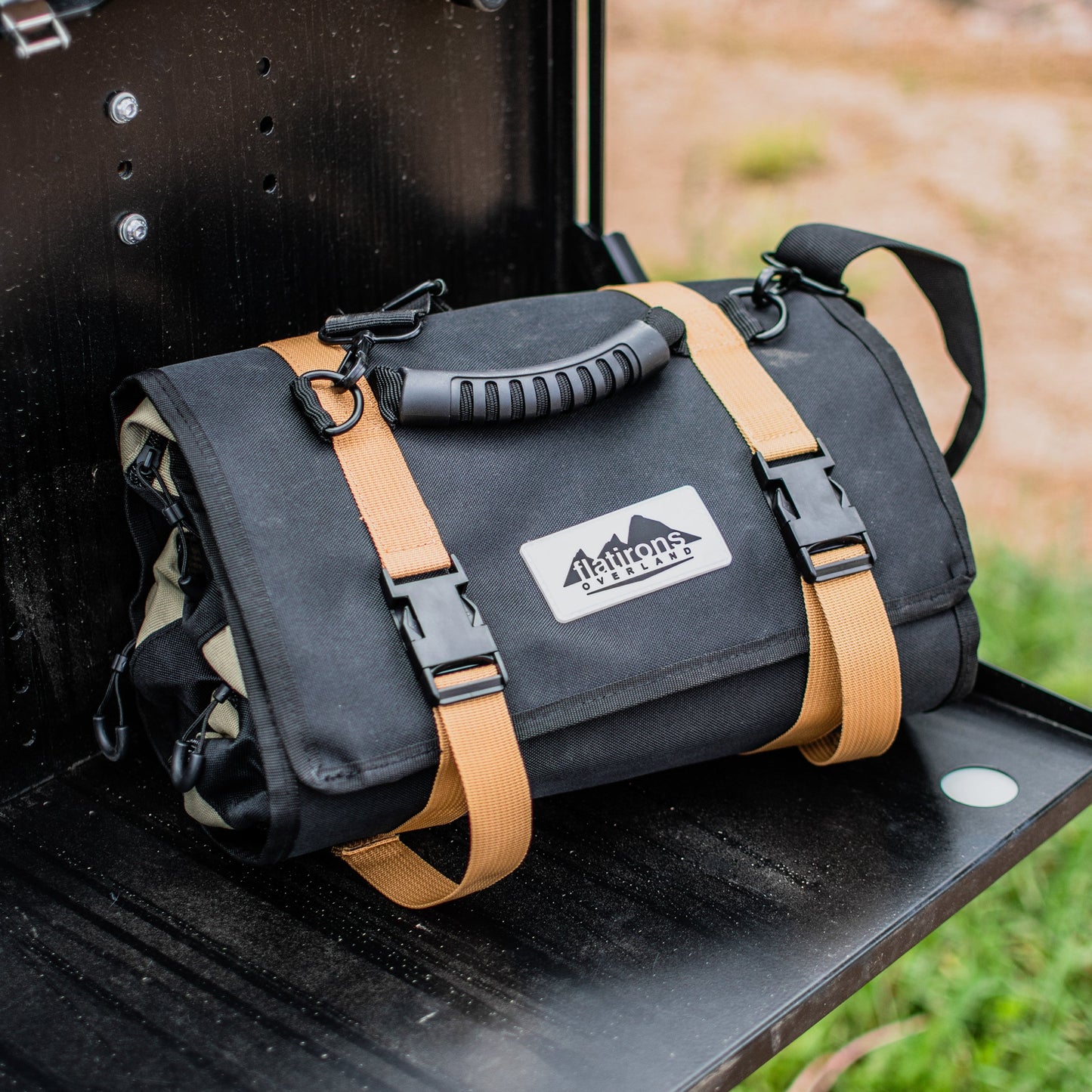 An AlphaLife247 modular gear roll with tan straps sitting on the tailgate of an overland vehicle, highlighting its compact, organized design for ready-to-use backcountry storage.
