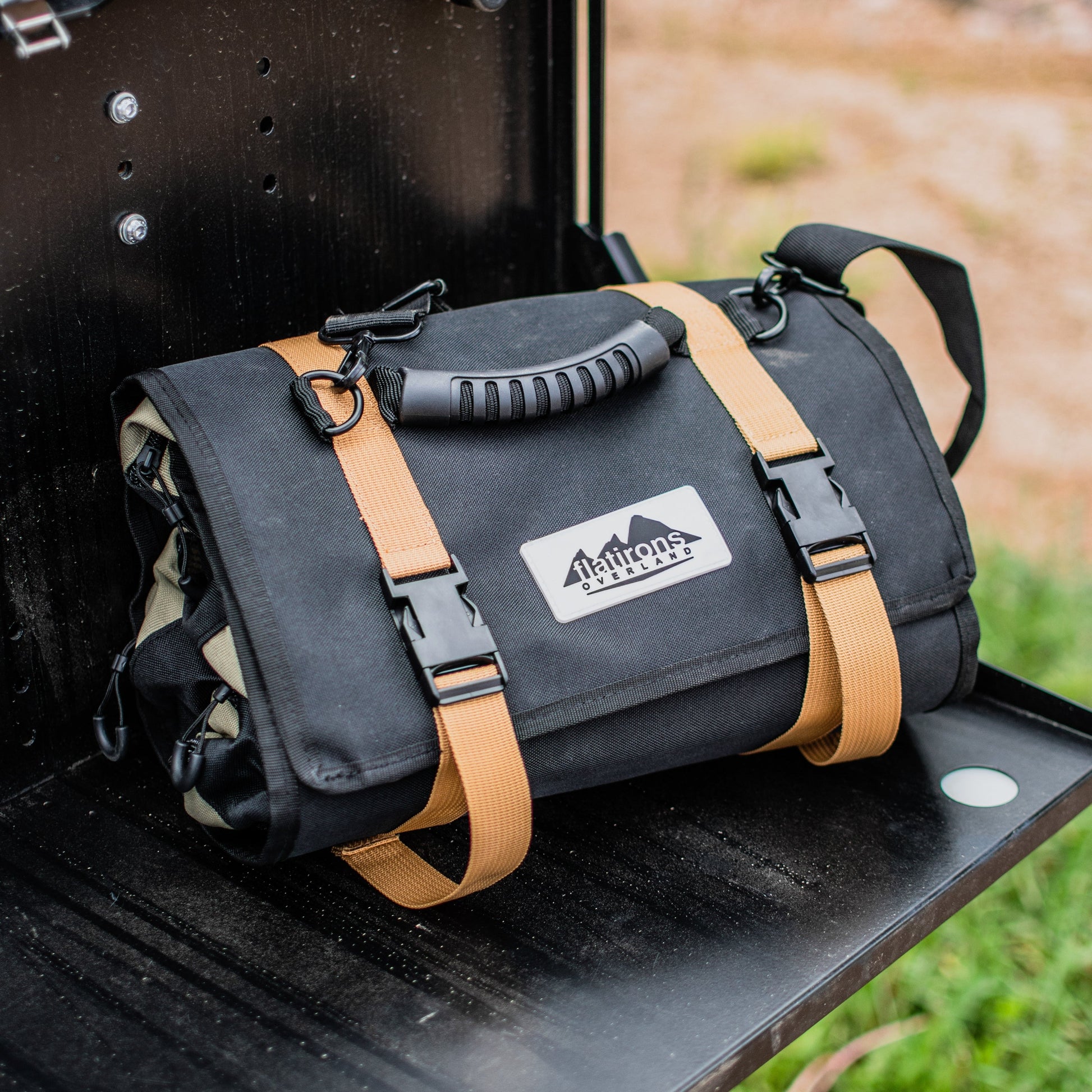 An AlphaLife247 modular gear roll with tan straps sitting on the tailgate of an overland vehicle, highlighting its compact, organized design for ready-to-use backcountry storage.